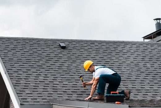 repairman in helmet holding hammer while repairing roof